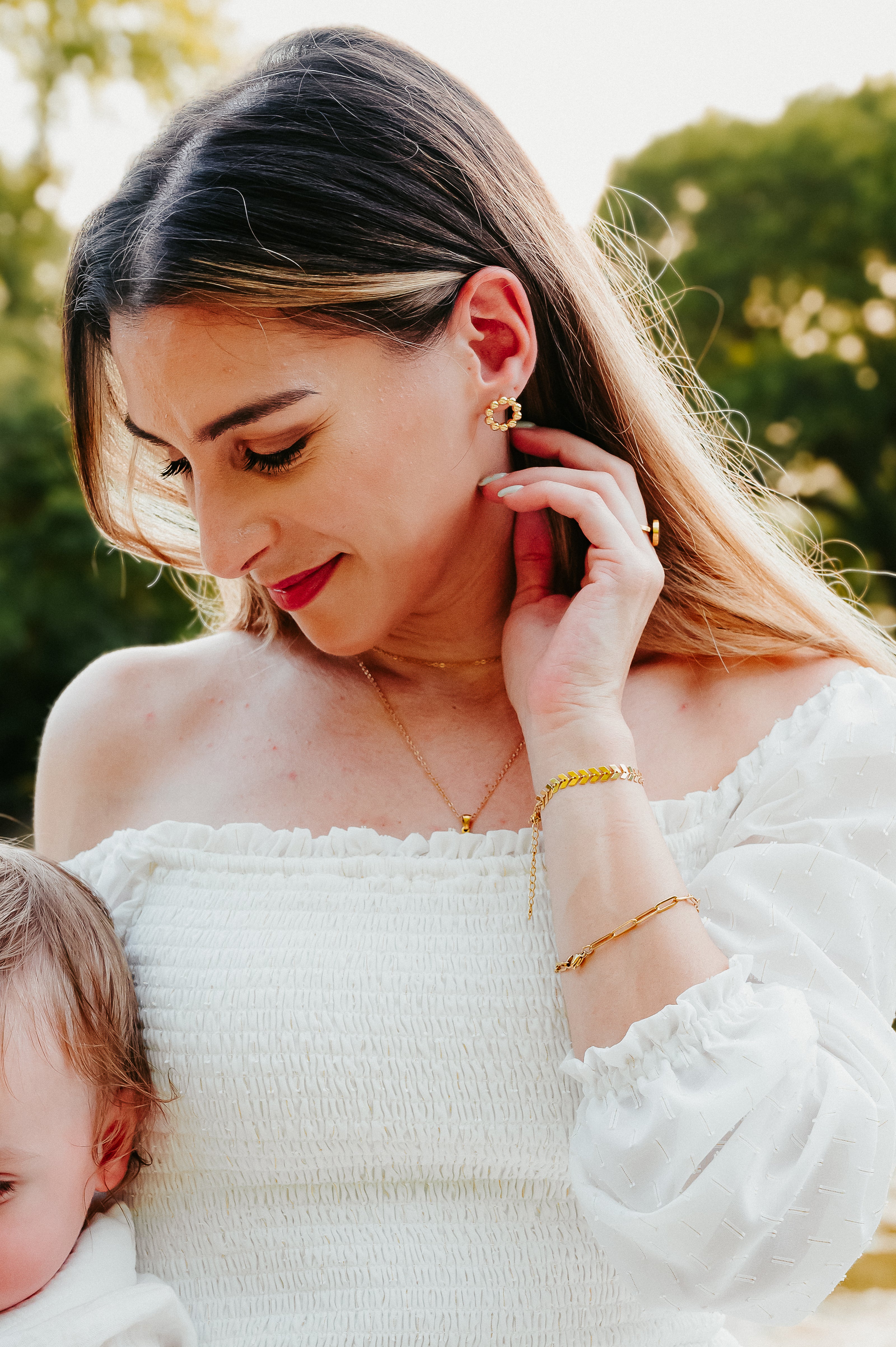 Woman adjusting earrings with a child in her arms outdoors