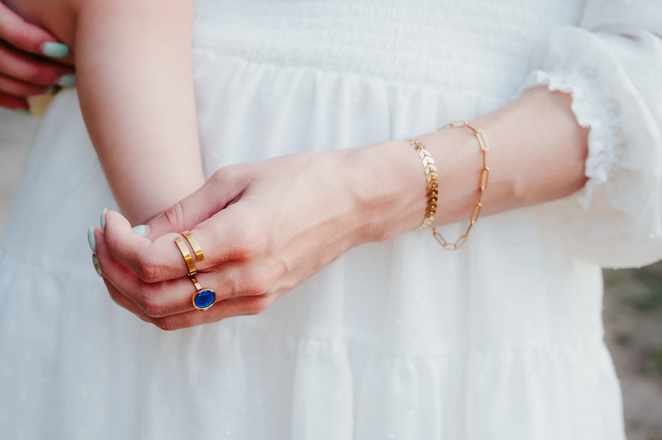 Close-up of a person's hand wearing gold rings and bracelets on a blurred background
