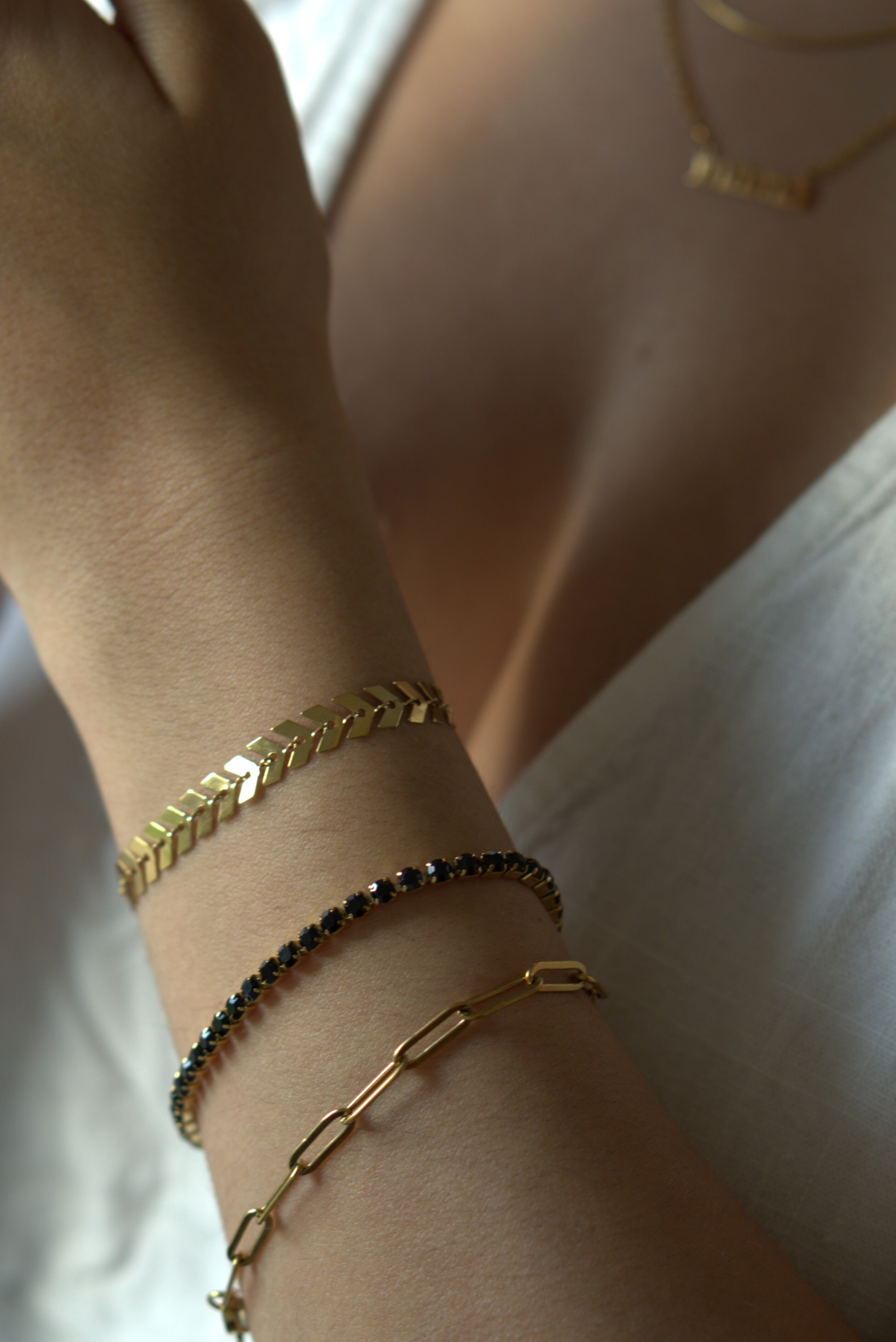 Close-up of a wrist wearing multiple gold bracelets on a blurred background
